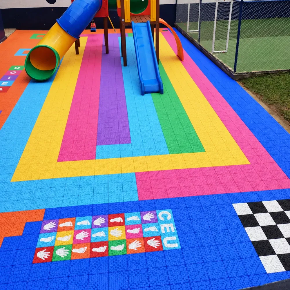 Área de brinquedos com faixas coloridas e jogos no piso modular